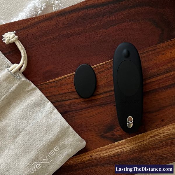 black we-vibe moxie+ remote control panty vibrator showing the magnet that secures the device to your underwear next to the fabric storage pouch