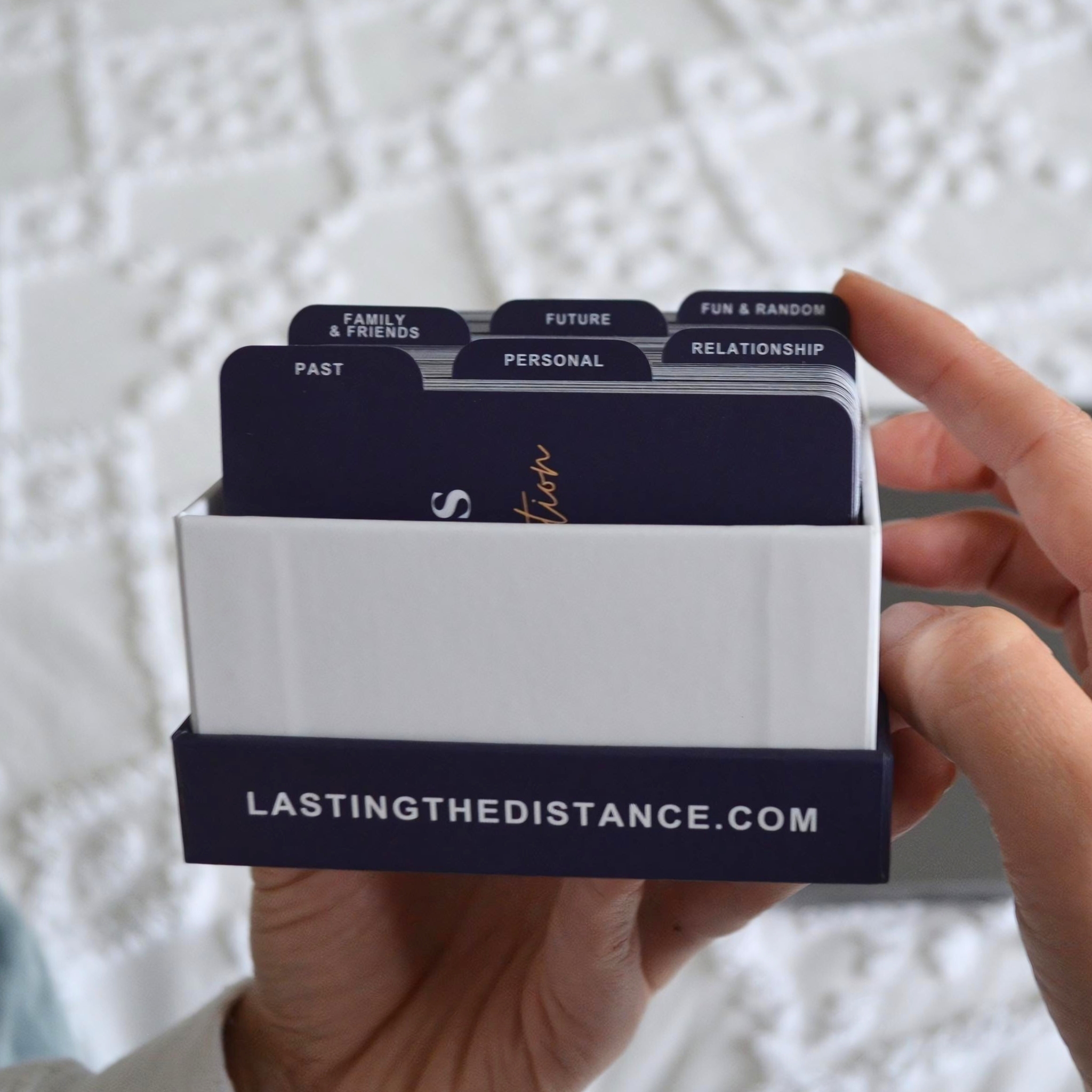 Person holding divided deck of cards labeled with various topics from 'lastingthedistance.com'.